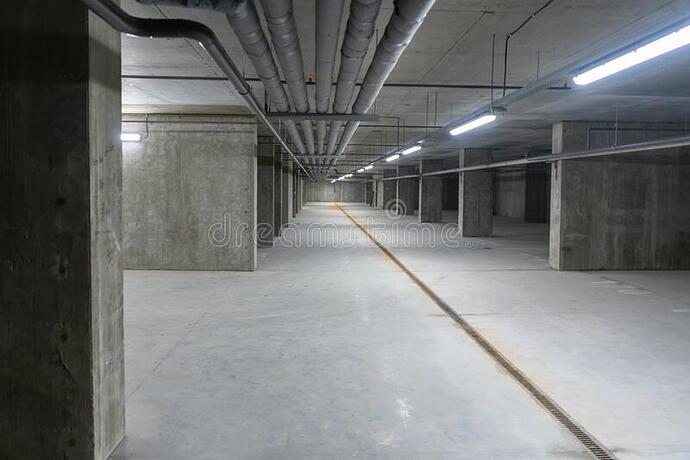 exposed-ceiling-pipes-commercial-basement-grey-concrete-receding-view-along-cement-corridor-driveway-lit-neon-lights-187651277